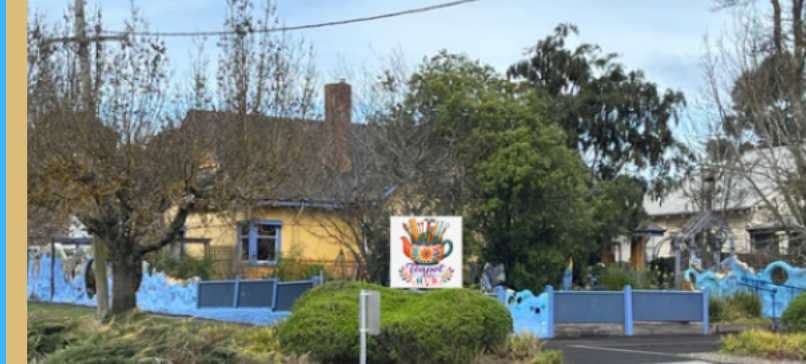 The Teapot Arts Hub building in Ballan: a yellow weatherboard house behind a blue picket fence, with the hub&rsquo;s teapot sign at the gate.