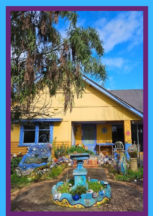 The garden at the hub: a blue mosaic fountain and planters in front of the yellow studio building.